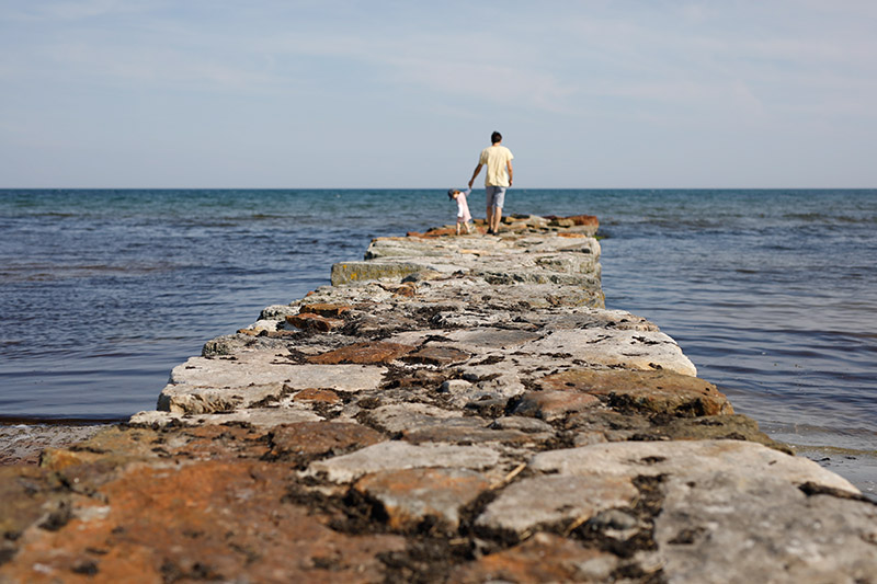 Ein Vater und seine Tochter laufen auf einem Steinweg raus aufs Meer auf Elternzeit in Dänemark.