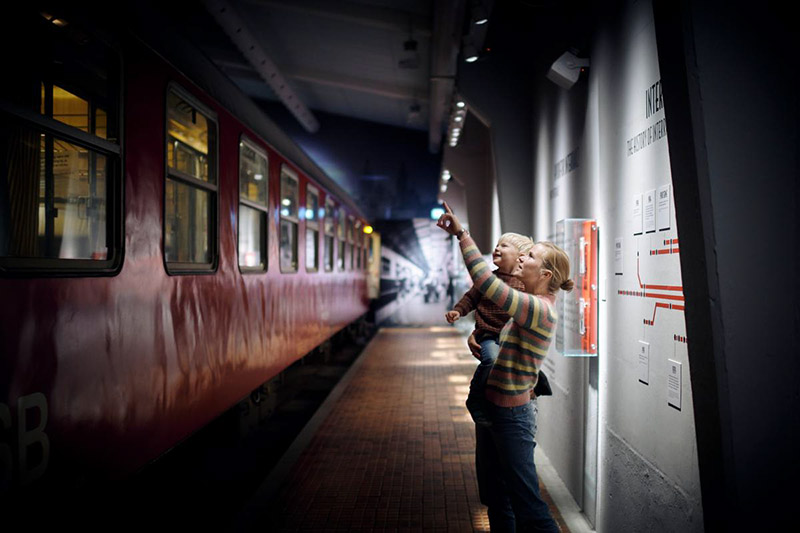 Eine Mutter hat ihr Kind auf dem Arm und steht am Bahnsteig für ihre Reise nach Dänemark mit Baby. 