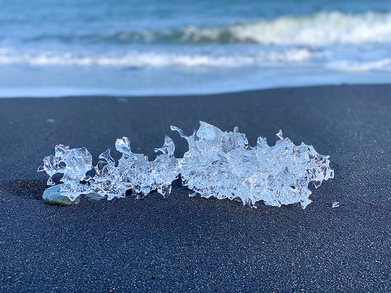 Ein Stück Eis auf schwarzem Sand.