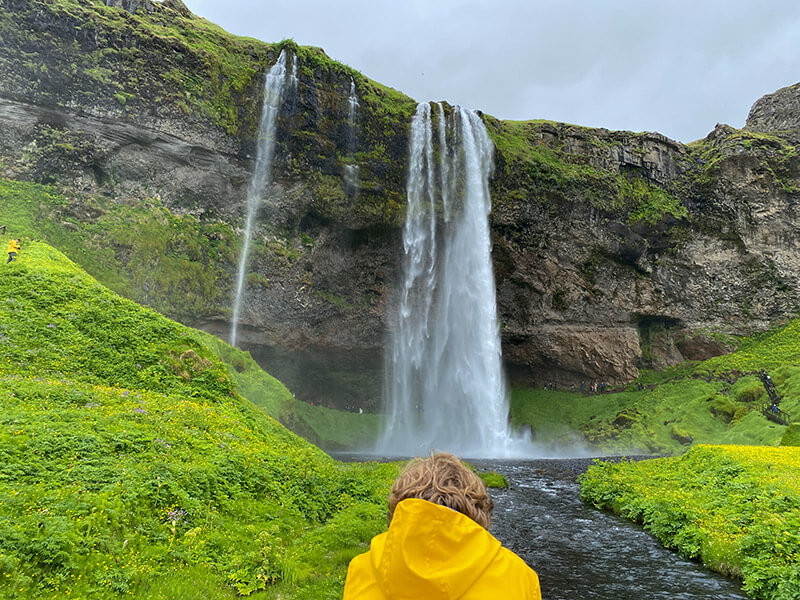 Ein Kind mit gelber Regenjacke steht vor einem Wasserfall