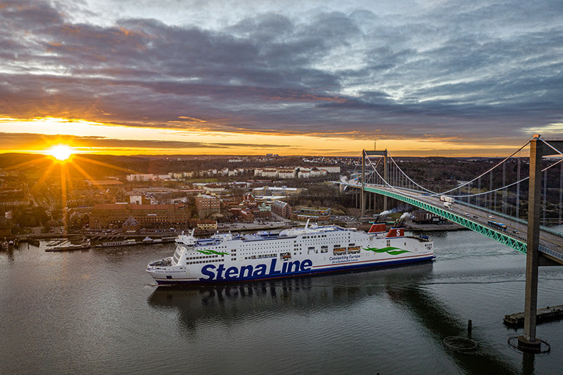 Fährschiff mit der Aufschrift 'Stena Line' fährt unter einer Hängebrücke bei Sonnenuntergang auf dem Meer vor Göteborg.
