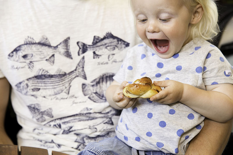 Ein kleines Kind hält eine Zimtschnecke in den Händen und strahlt.